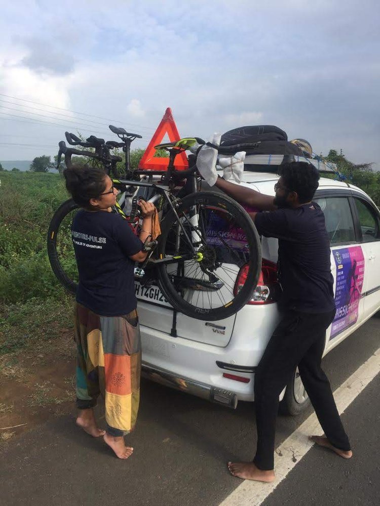 Jyoti Tripathi and a crew member strapping a bicycle to the roof rack of the support vehicle at the roadside